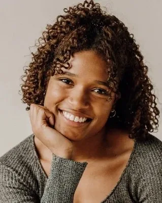 Jade Cameron, smiling with her chin resting on her hand, in a grey knit top.