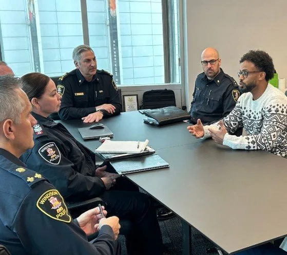 Mehari Hagos in conversation with uniformed Windsor Police Service officers around a boardroom table.