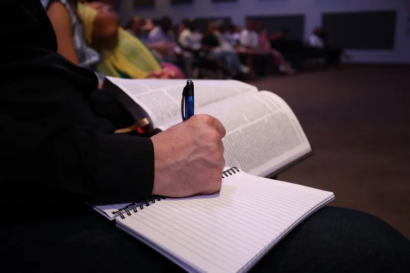 Hands writing in a notebook beside an open book during a leadership session.