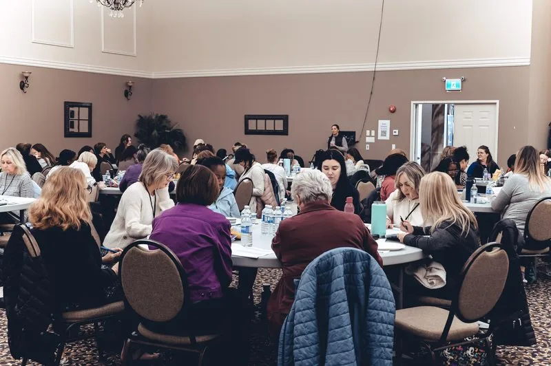 A room of participants at round tables during a leadership training day.