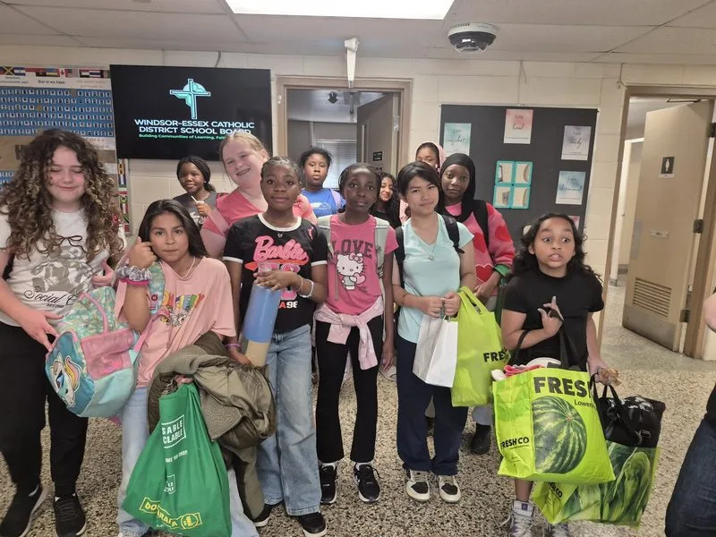 Young people in a school hallway carrying bags of groceries and supplies from a community outreach night.