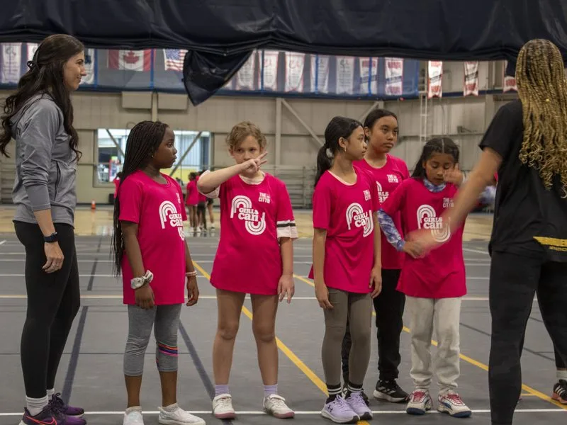 Two coaches in conversation with a group of girls in matching shirts at a sports clinic.