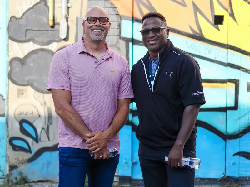 Two community leaders standing side by side in front of a painted mural.