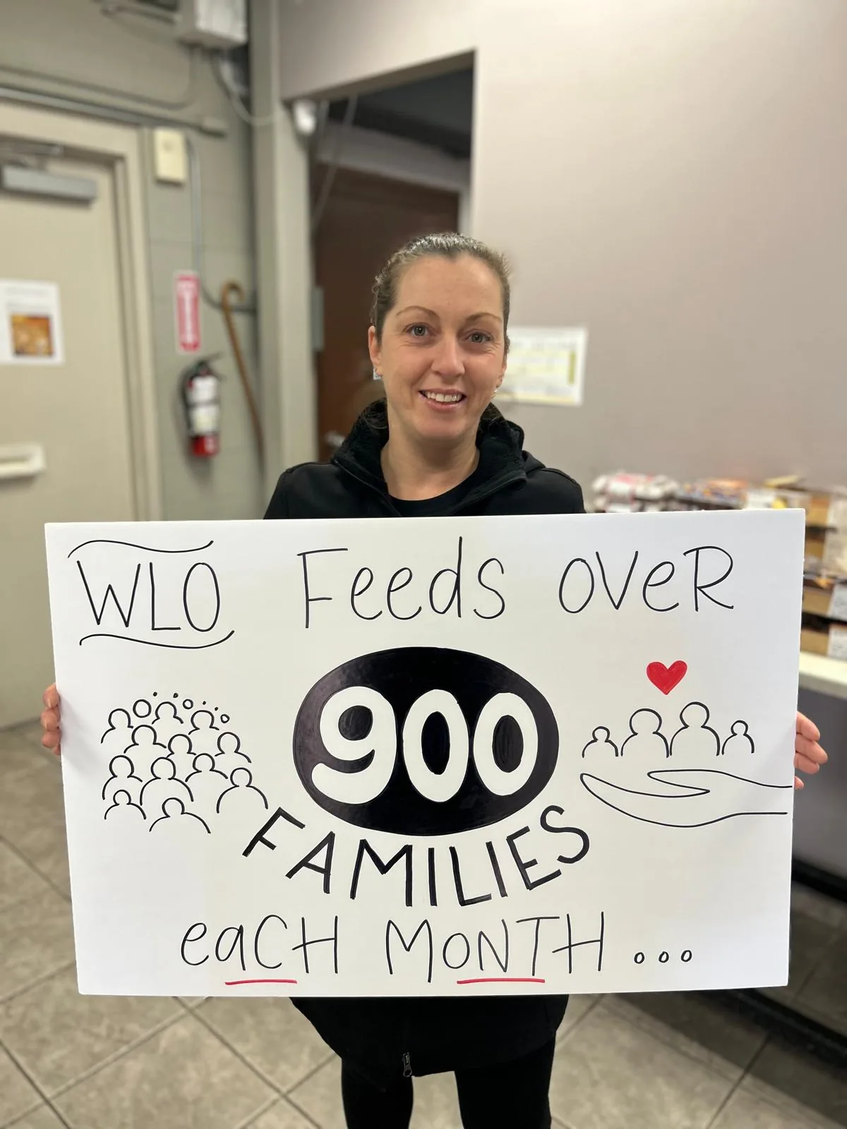 A volunteer at Windsor Lifeline Outreach holding a hand-drawn sign that reads WLO feeds over 900 families each month.