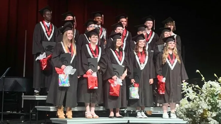 Maranatha Christian Academy Class of 2025 graduates standing together on stage in caps and gowns.